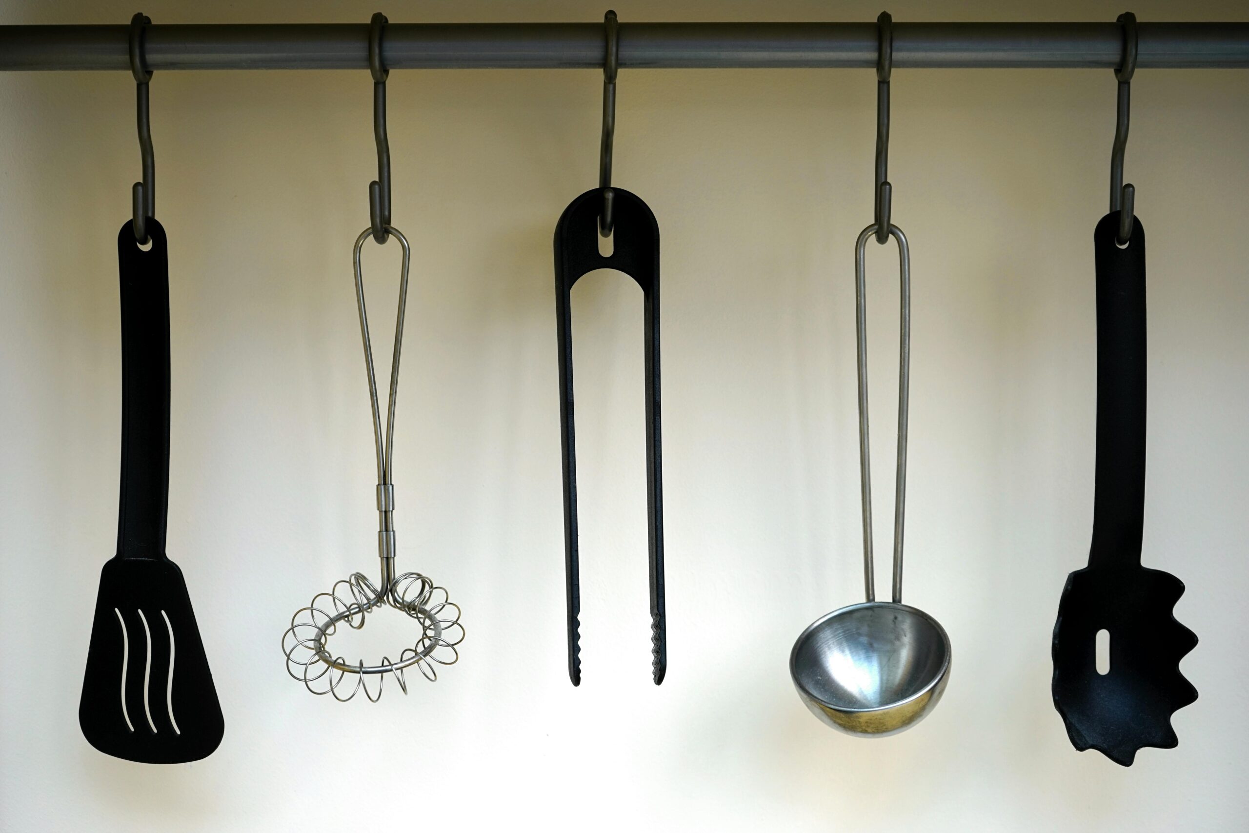 A set of stainless steel and plastic kitchen utensils hanging on a rail.